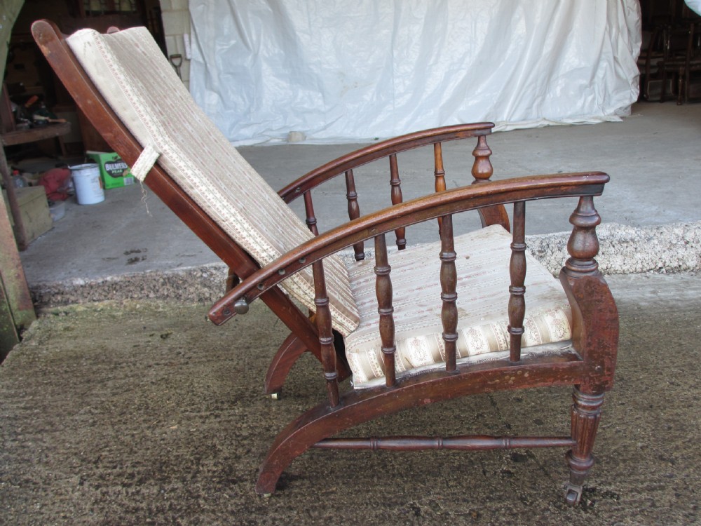 A 19th-century dark mahogany armchair featuring turned side spindles, beige striped upholstery, an adjustable reclining backrest, and brass castors. View X