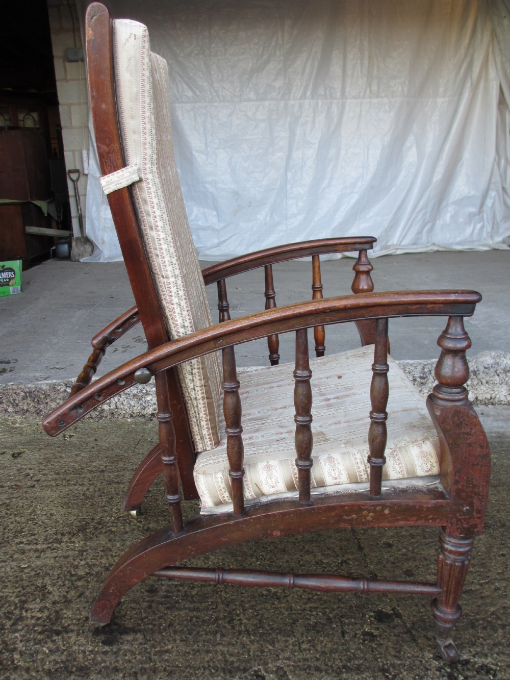 A 19th-century dark mahogany armchair featuring turned side spindles, beige striped upholstery, an adjustable reclining backrest, and brass castors. View XI