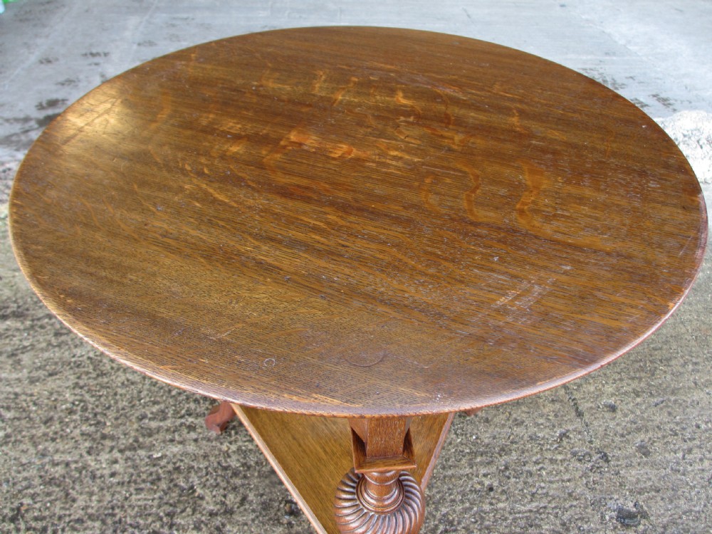 An Edwardian oak circular occasional table featuring three carved spiral-bulb legs, a shaped apron, and a lower triangular tier shelf. View II