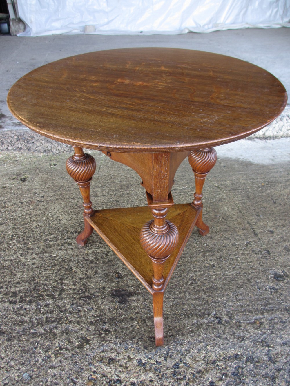 An Edwardian oak circular occasional table featuring three carved spiral-bulb legs, a shaped apron, and a lower triangular tier shelf. View IV