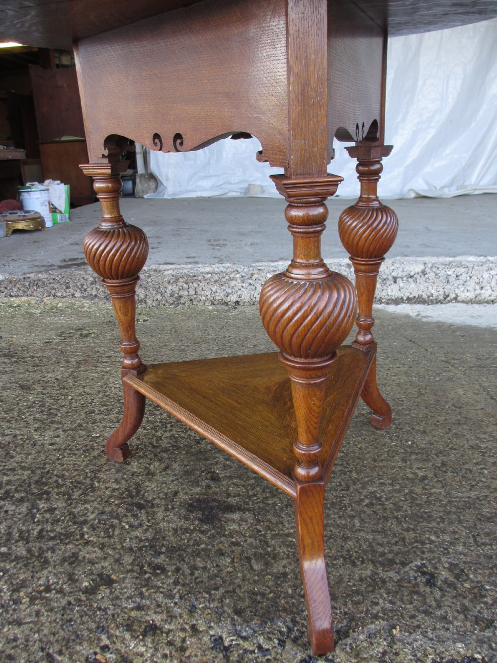 An Edwardian oak circular occasional table featuring three carved spiral-bulb legs, a shaped apron, and a lower triangular tier shelf. View V