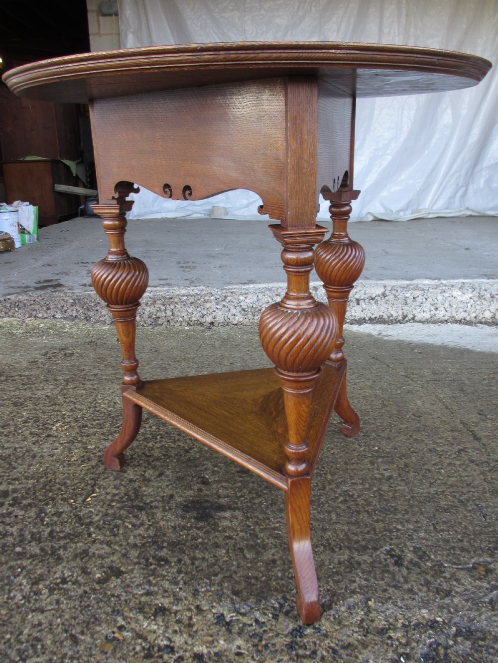 An Edwardian oak circular occasional table featuring three carved spiral-bulb legs, a shaped apron, and a lower triangular tier shelf. View VI