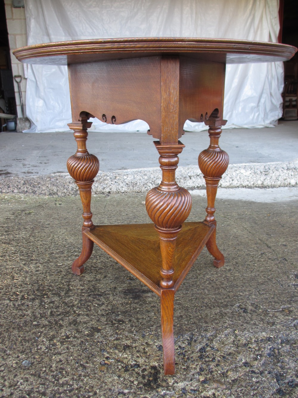 An Edwardian oak circular occasional table featuring three carved spiral-bulb legs, a shaped apron, and a lower triangular tier shelf. View VII
