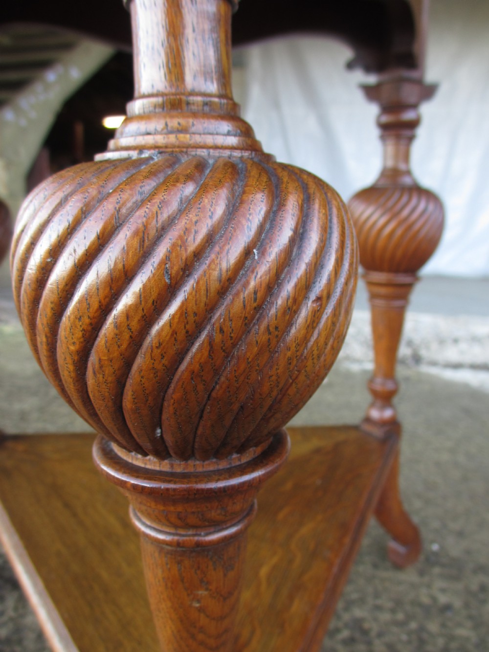 An Edwardian oak circular occasional table featuring three carved spiral-bulb legs, a shaped apron, and a lower triangular tier shelf. View X
