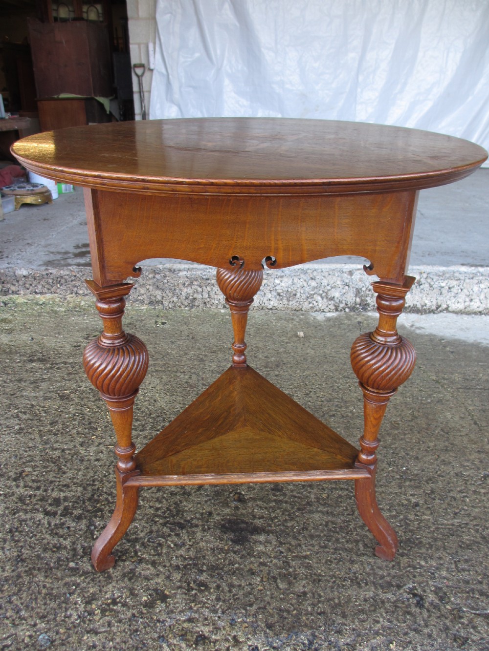 An Edwardian oak circular occasional table featuring three carved spiral-bulb legs, a shaped apron, and a lower triangular tier shelf. View XIV