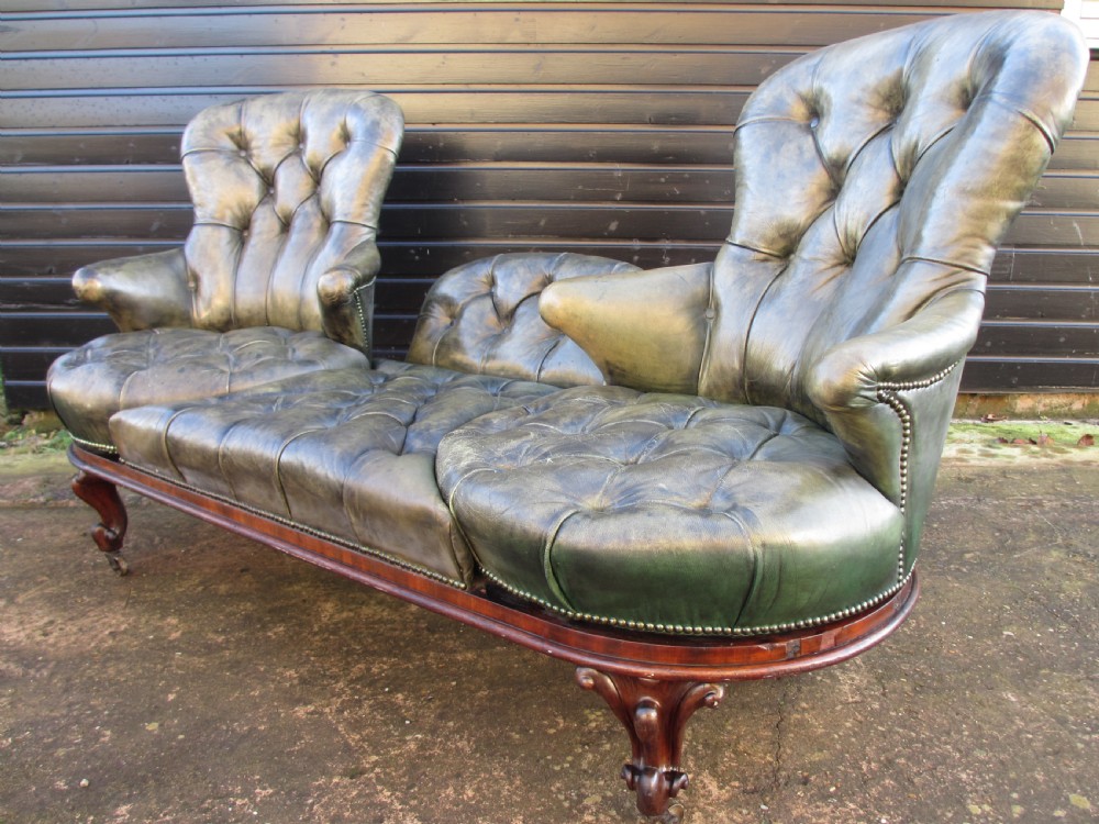 A Victorian conversation sofa upholstered in buttoned dark green leather featuring a carved rosewood frame with brass castors. View II