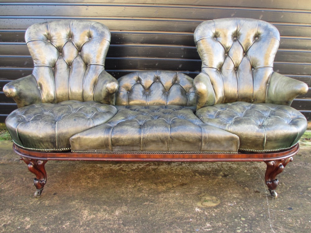 A Victorian conversation sofa upholstered in buttoned dark green leather featuring a carved rosewood frame with brass castors. View III
