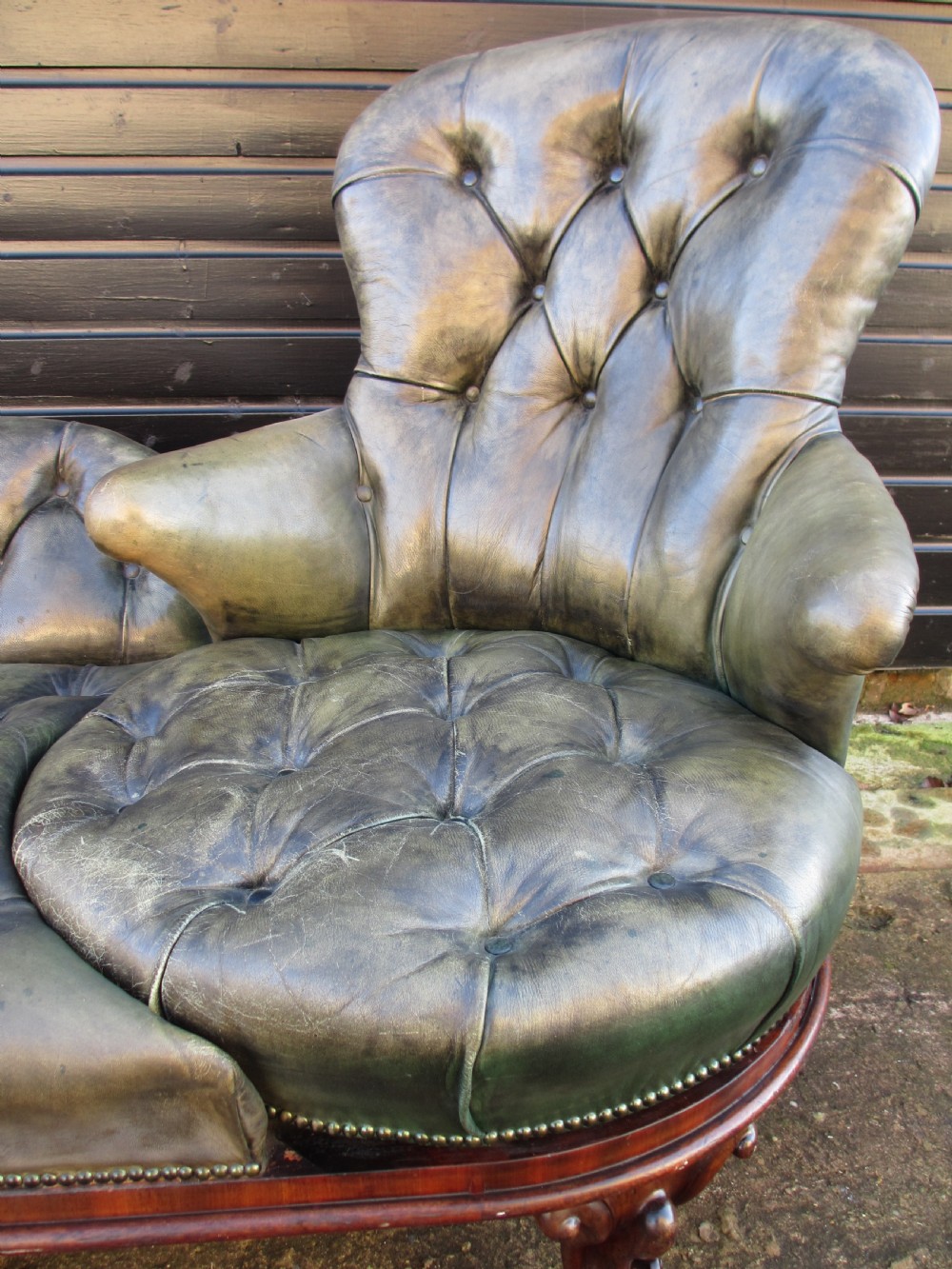 A Victorian conversation sofa upholstered in buttoned dark green leather featuring a carved rosewood frame with brass castors. View V
