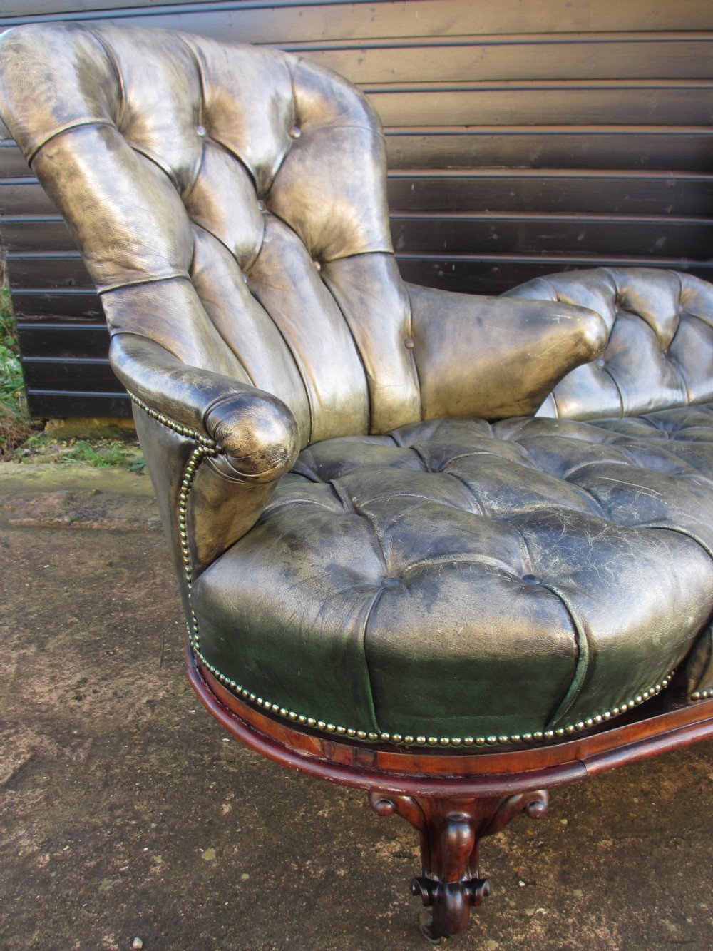 A Victorian conversation sofa upholstered in buttoned dark green leather featuring a carved rosewood frame with brass castors. View VI