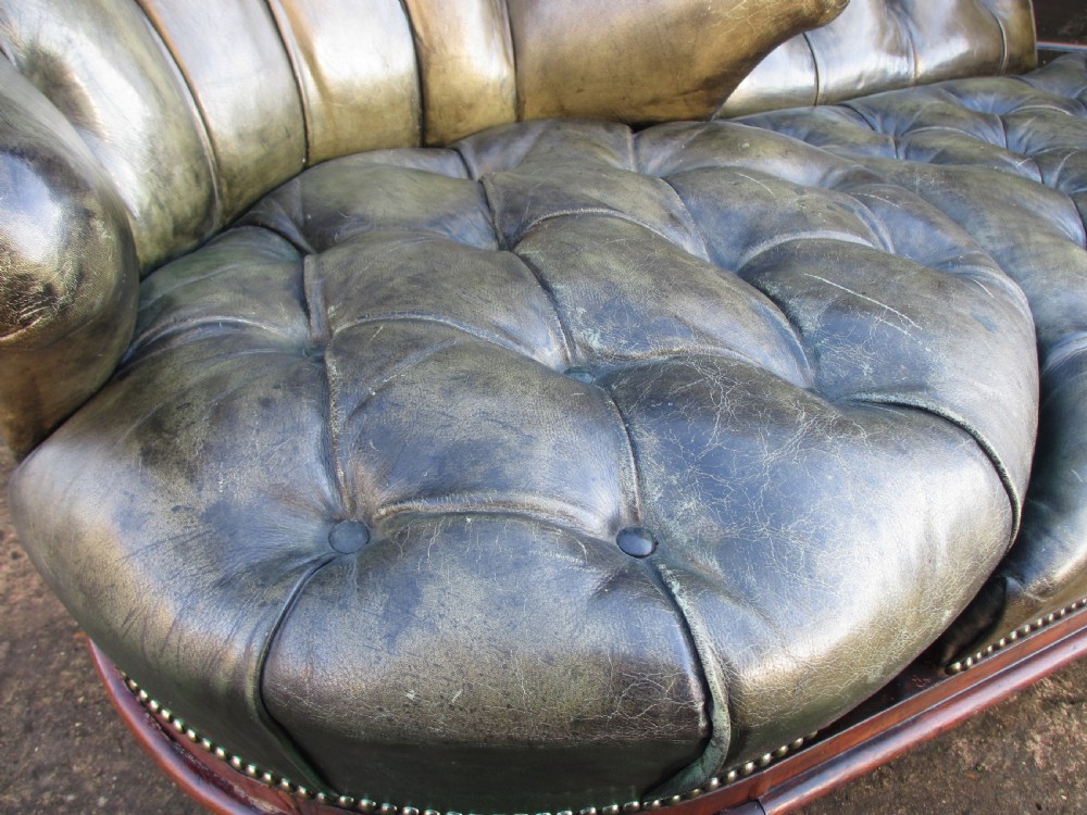 A Victorian conversation sofa upholstered in buttoned dark green leather featuring a carved rosewood frame with brass castors. View IX