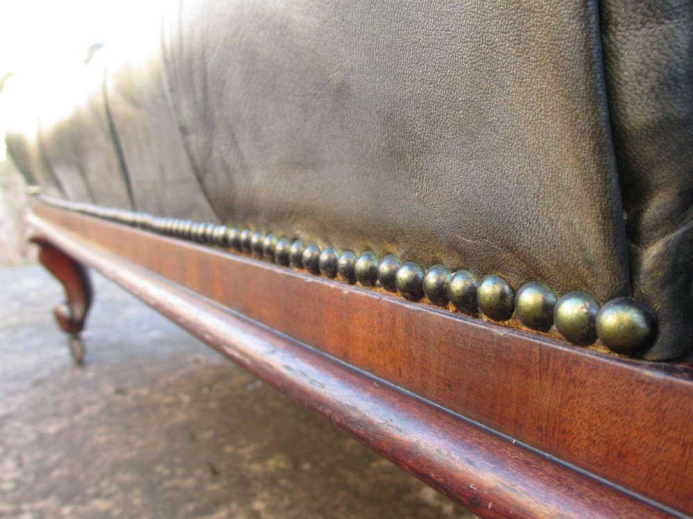 A Victorian conversation sofa upholstered in buttoned dark green leather featuring a carved rosewood frame with brass castors. View X