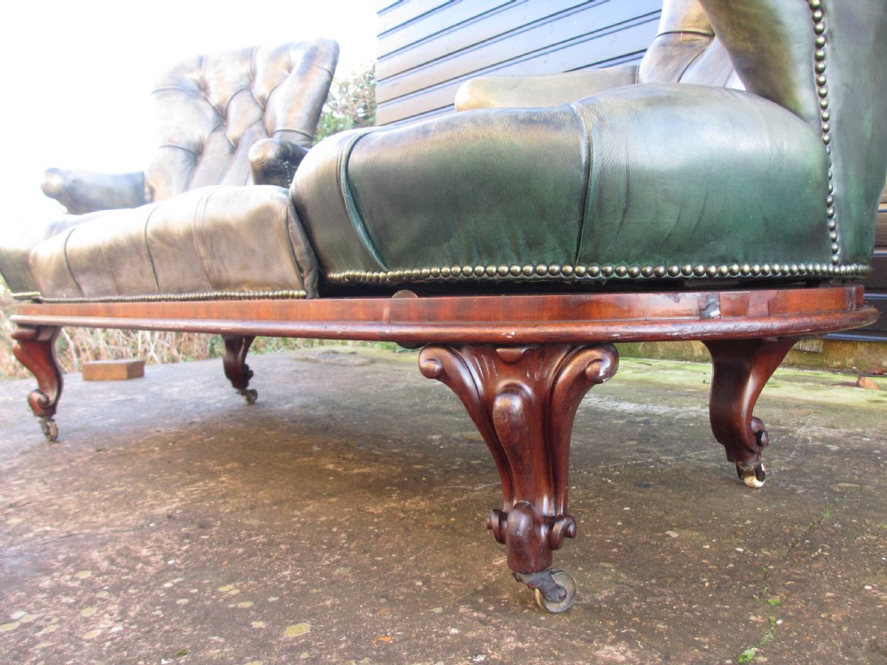 A Victorian conversation sofa upholstered in buttoned dark green leather featuring a carved rosewood frame with brass castors. View XIII