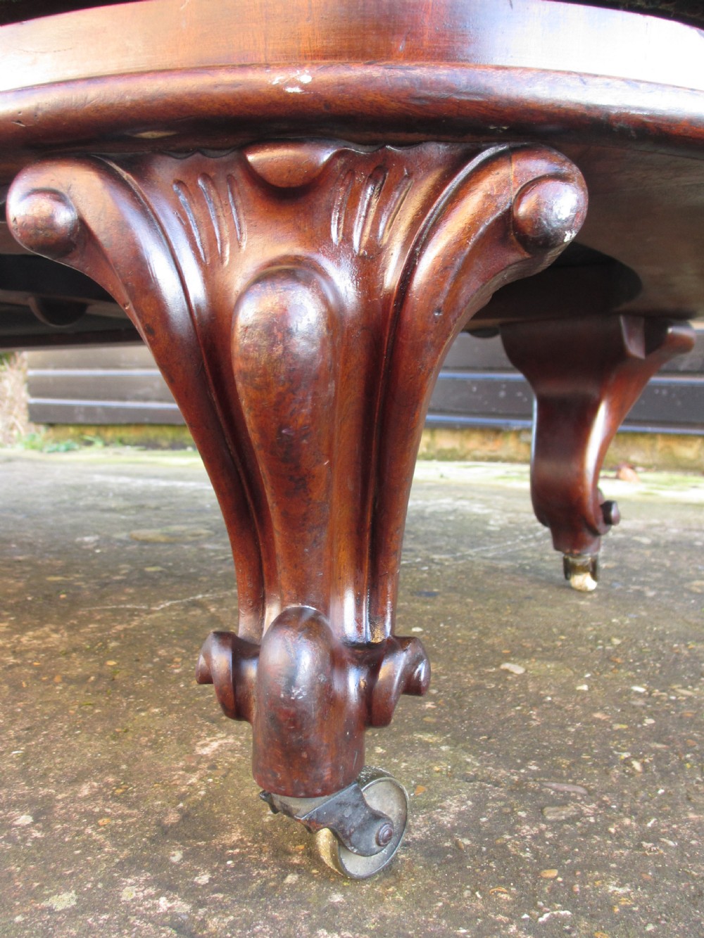 A Victorian conversation sofa upholstered in buttoned dark green leather featuring a carved rosewood frame with brass castors. View XIV