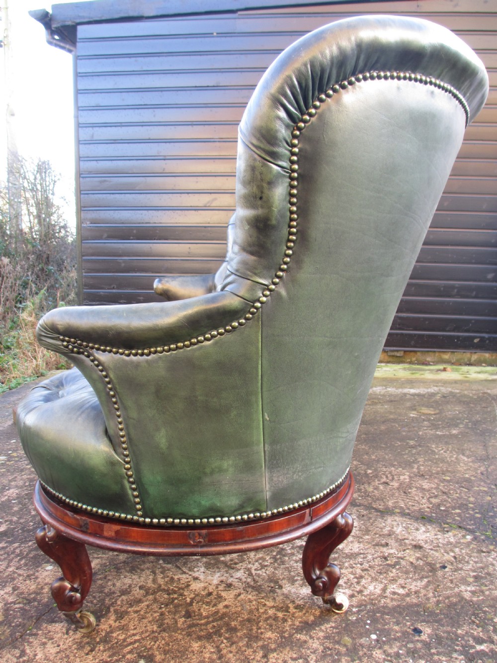 A Victorian conversation sofa upholstered in buttoned dark green leather featuring a carved rosewood frame with brass castors. View XV