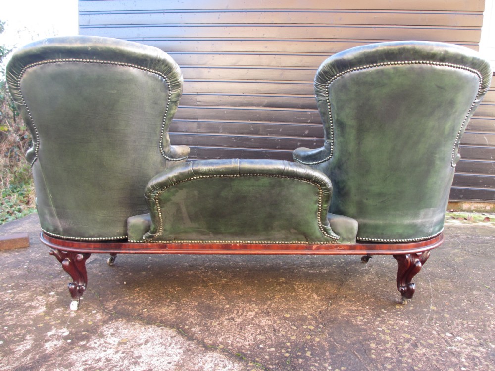 A Victorian conversation sofa upholstered in buttoned dark green leather featuring a carved rosewood frame with brass castors. View XVI
