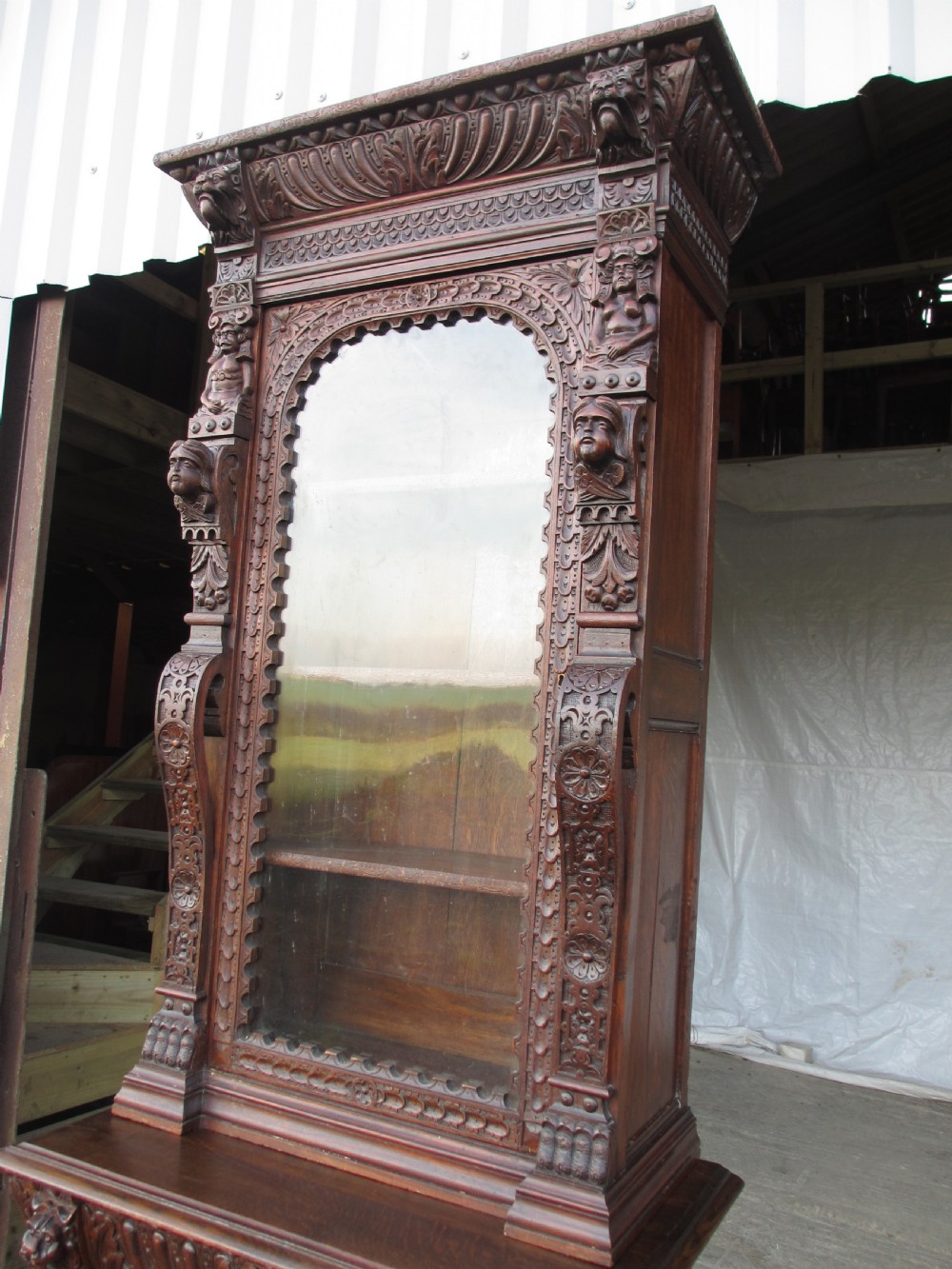 A tall two-part dark oak Victorian bookcase featuring an arched glazed upper door, carved face motifs, and geometric panelled lower drawers. View II