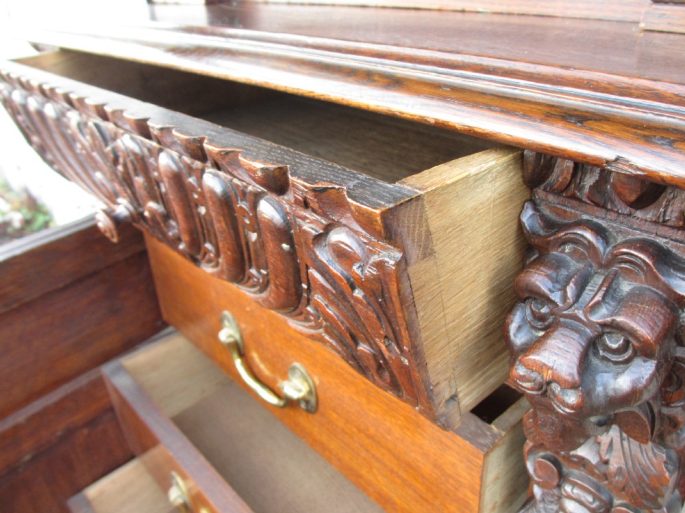 A tall two-part dark oak Victorian bookcase featuring an arched glazed upper door, carved face motifs, and geometric panelled lower drawers. View VI