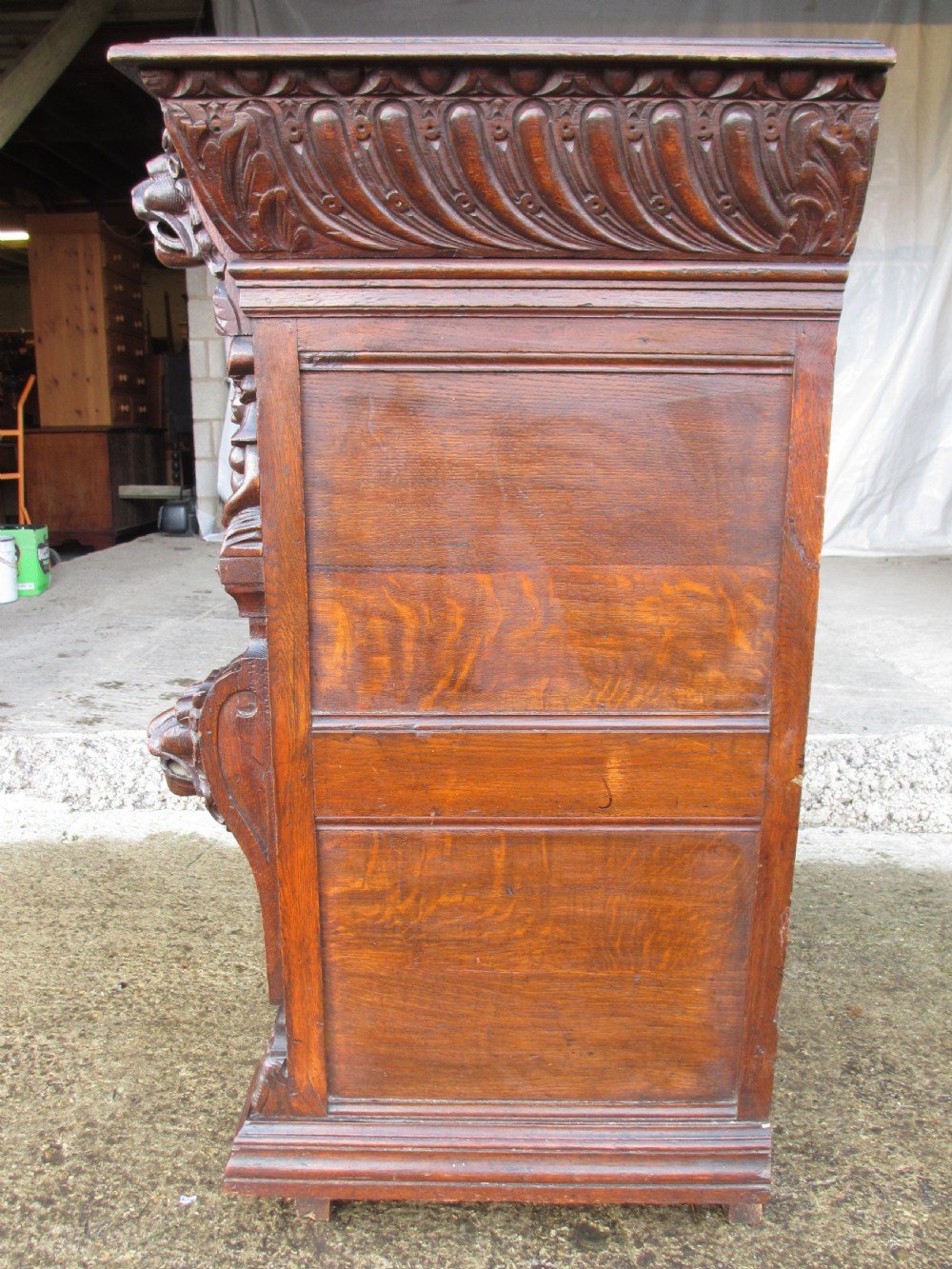 A tall two-part dark oak Victorian bookcase featuring an arched glazed upper door, carved face motifs, and geometric panelled lower drawers. View VII