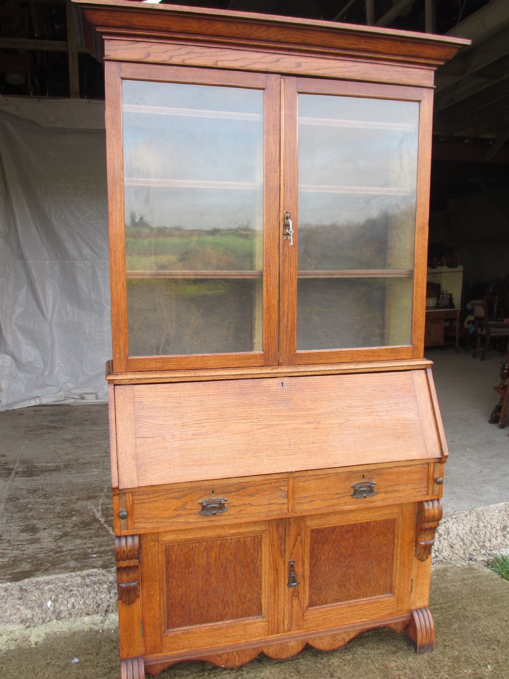 An Edwardian golden oak bureau bookcase featuring a two-door glazed upper section, a fall-front slanted writing desk, and a lower cabinet base with carved supports.
