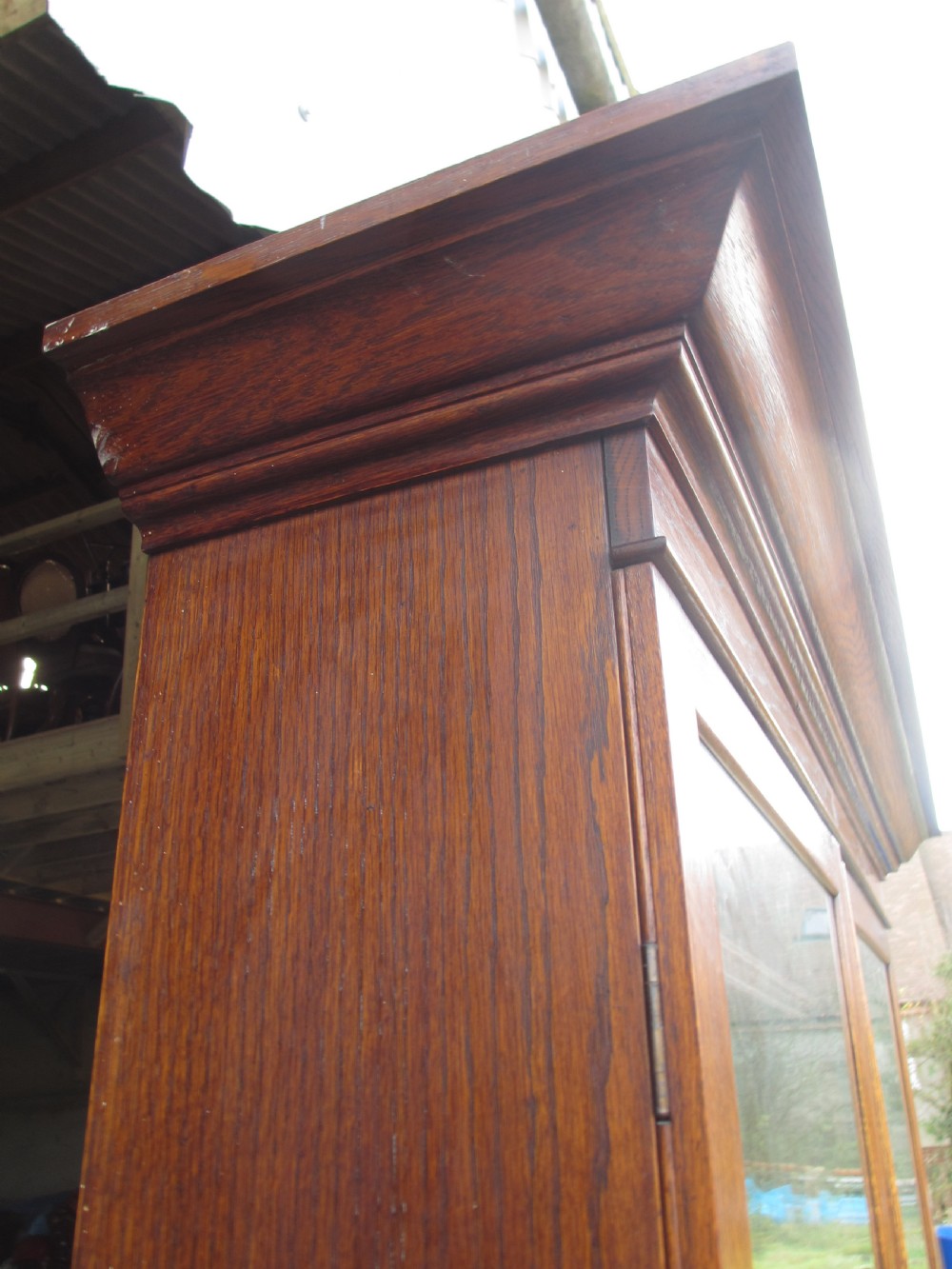 An Edwardian golden oak bureau bookcase featuring a two-door glazed upper section, a fall-front slanted writing desk, and a lower cabinet base with carved supports. View II