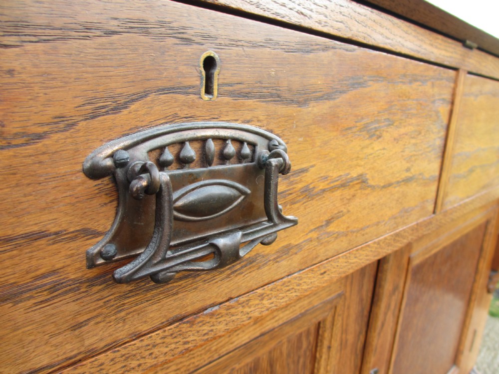 An Edwardian golden oak bureau bookcase featuring a two-door glazed upper section, a fall-front slanted writing desk, and a lower cabinet base with carved supports. View V
