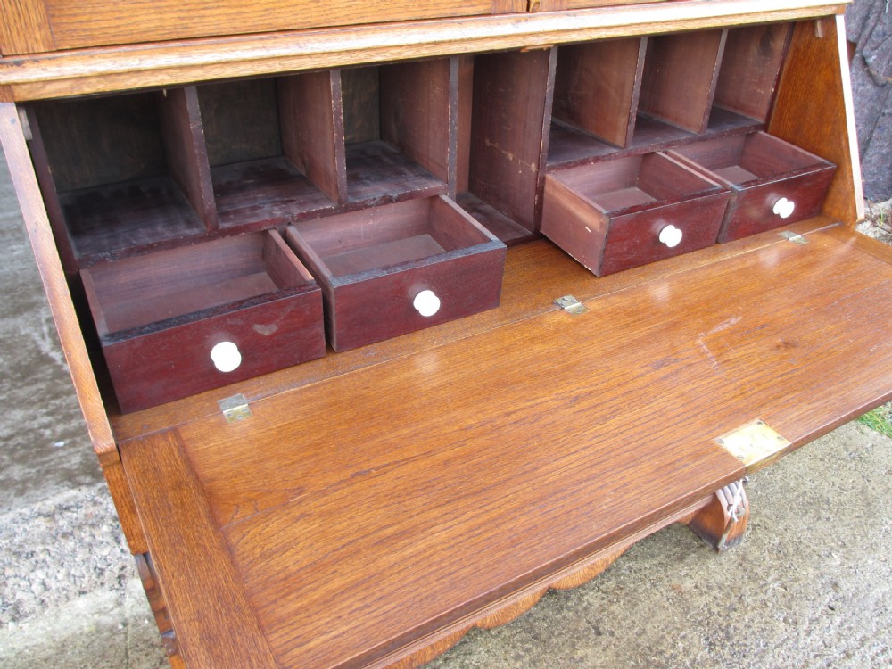 An Edwardian golden oak bureau bookcase featuring a two-door glazed upper section, a fall-front slanted writing desk, and a lower cabinet base with carved supports. View VII