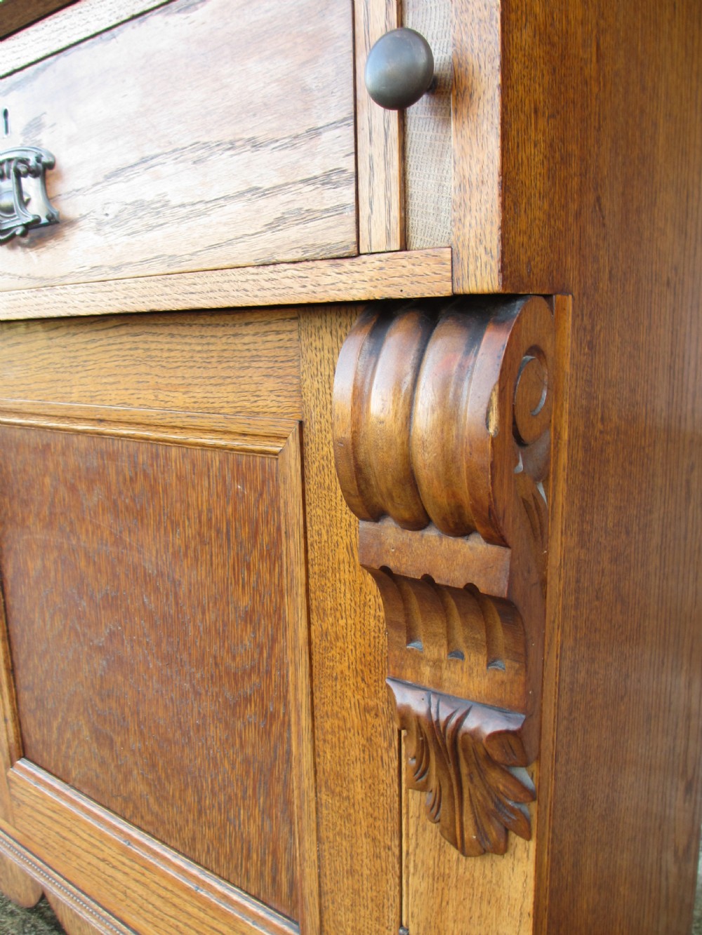 An Edwardian golden oak bureau bookcase featuring a two-door glazed upper section, a fall-front slanted writing desk, and a lower cabinet base with carved supports. View X