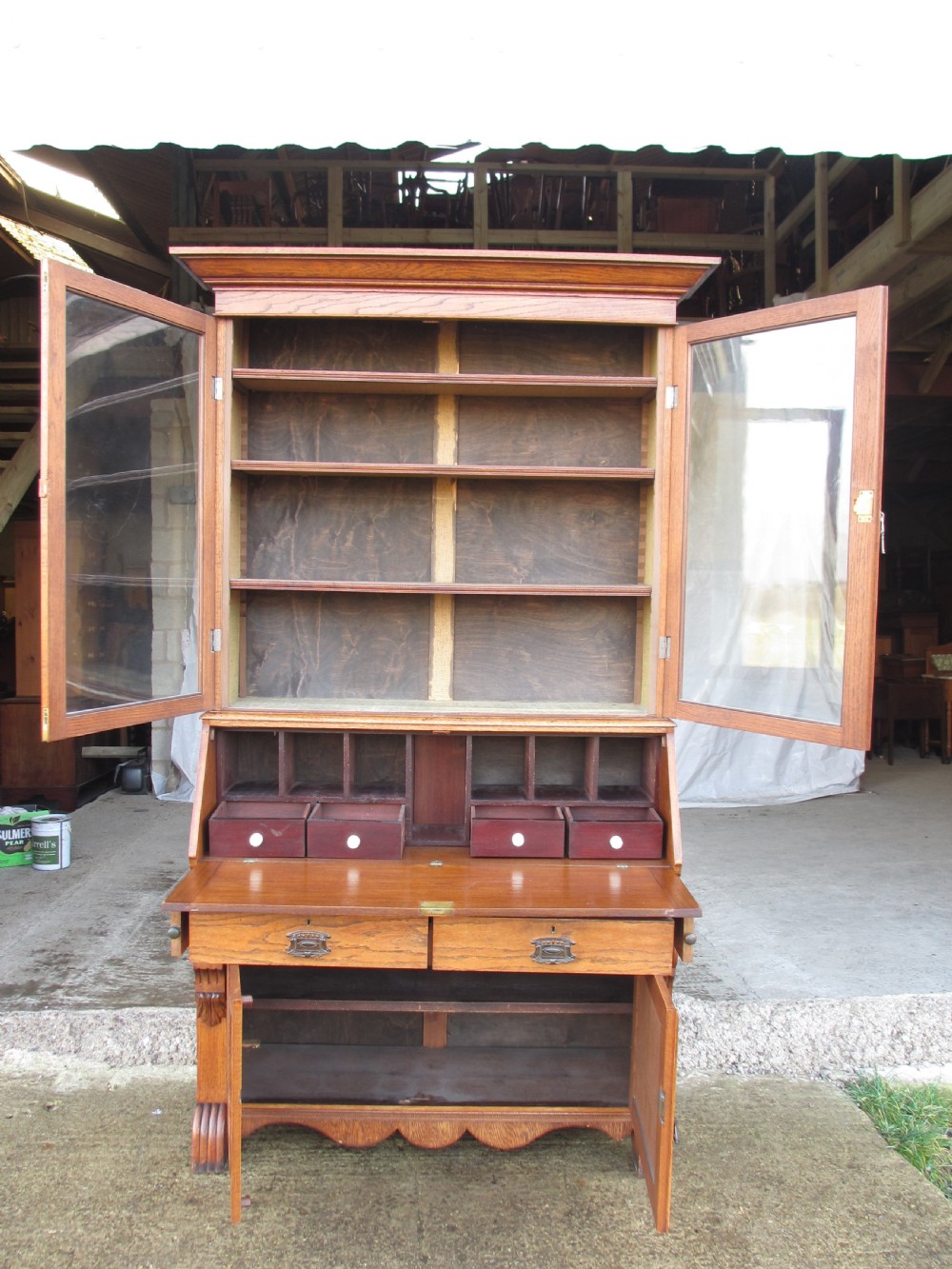 An Edwardian golden oak bureau bookcase featuring a two-door glazed upper section, a fall-front slanted writing desk, and a lower cabinet base with carved supports. View XI