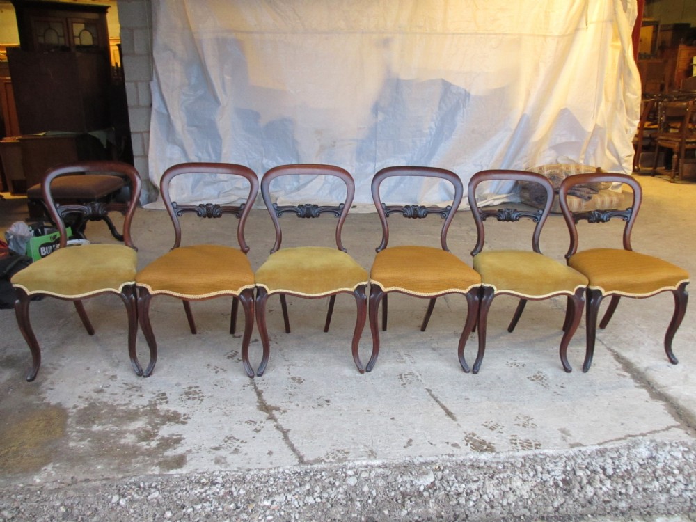 A set of six Victorian rosewood balloon back dining chairs with carved waist rails, yellow upholstered serpentine seats, and cabriole legs.