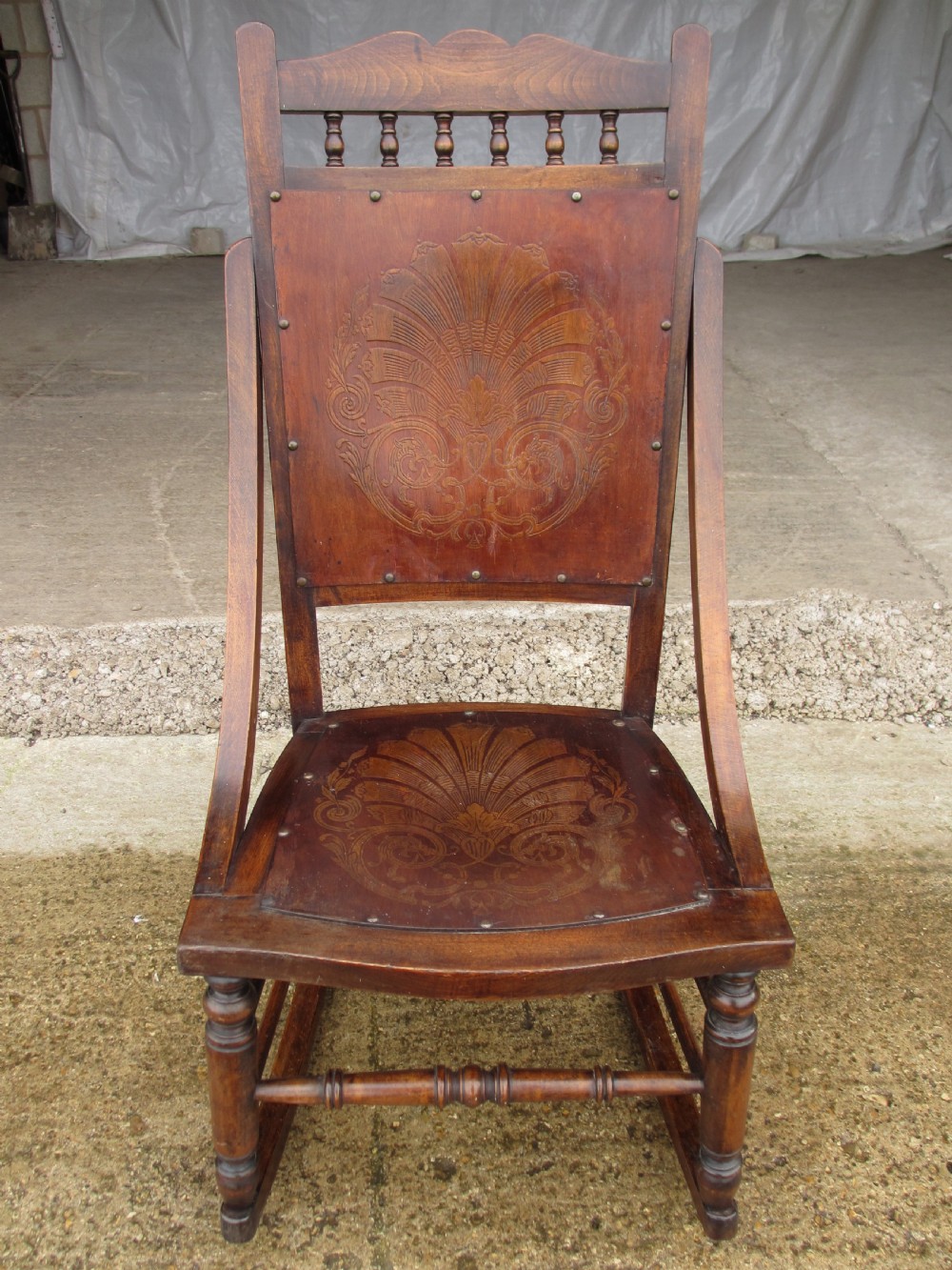 A Victorian oak and beech rocking chair featuring turned spindles, a carved shell pattern on the backrest and seat, and decorative metal studs.
