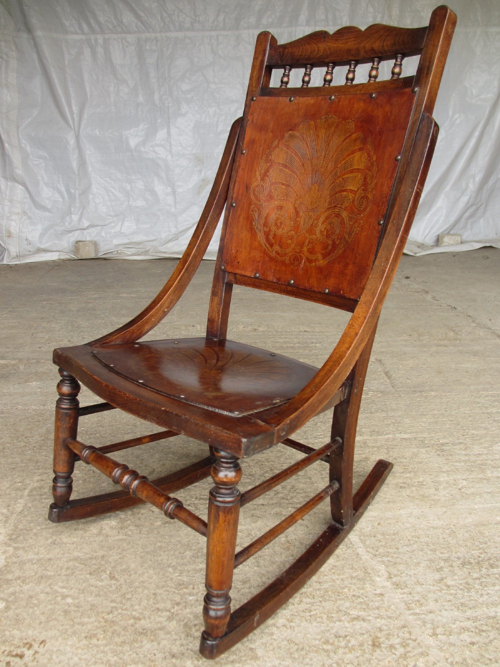 A Victorian oak and beech rocking chair featuring turned spindles, a carved shell pattern on the backrest and seat, and decorative metal studs. View II
