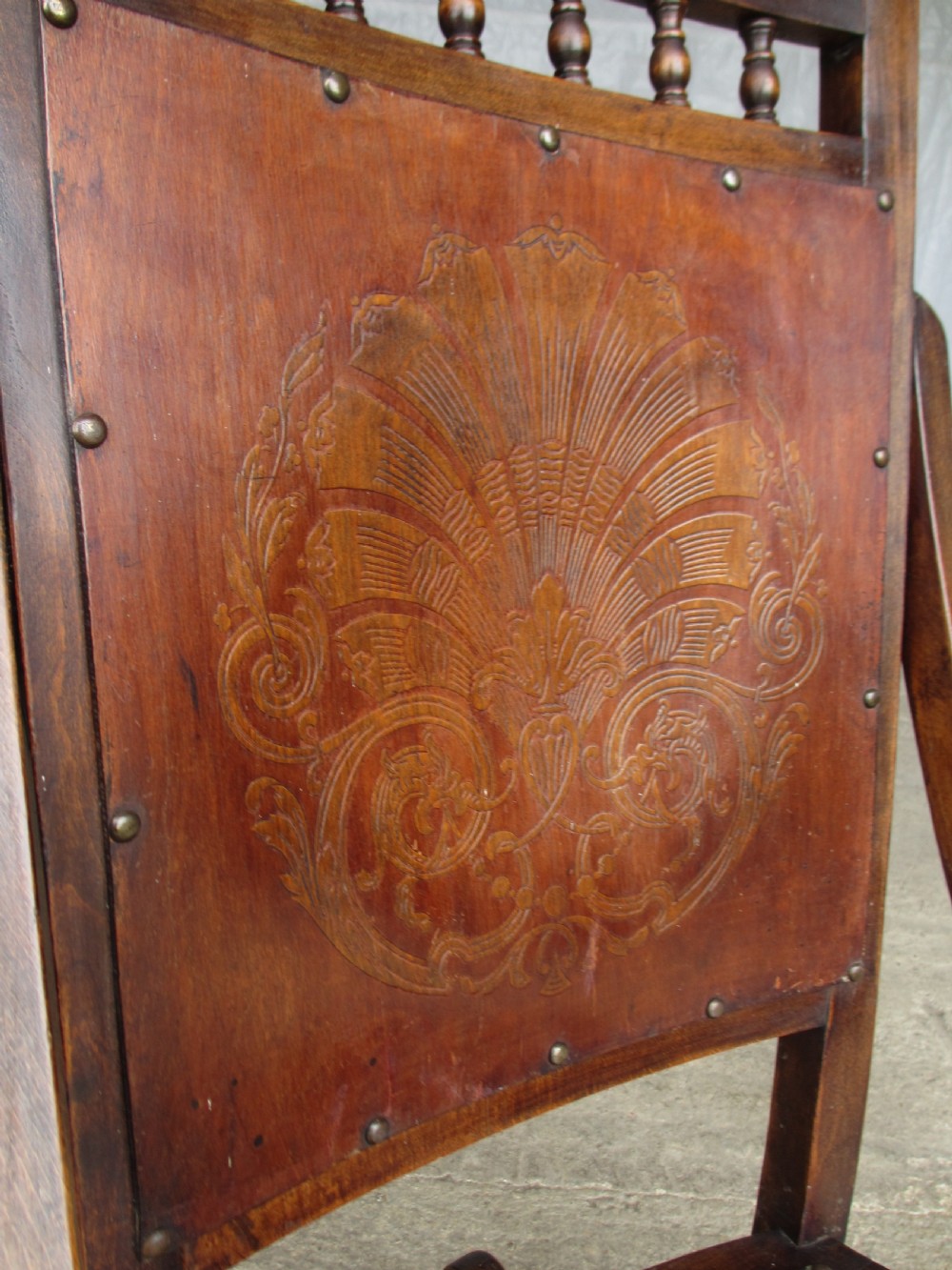 A Victorian oak and beech rocking chair featuring turned spindles, a carved shell pattern on the backrest and seat, and decorative metal studs. View V