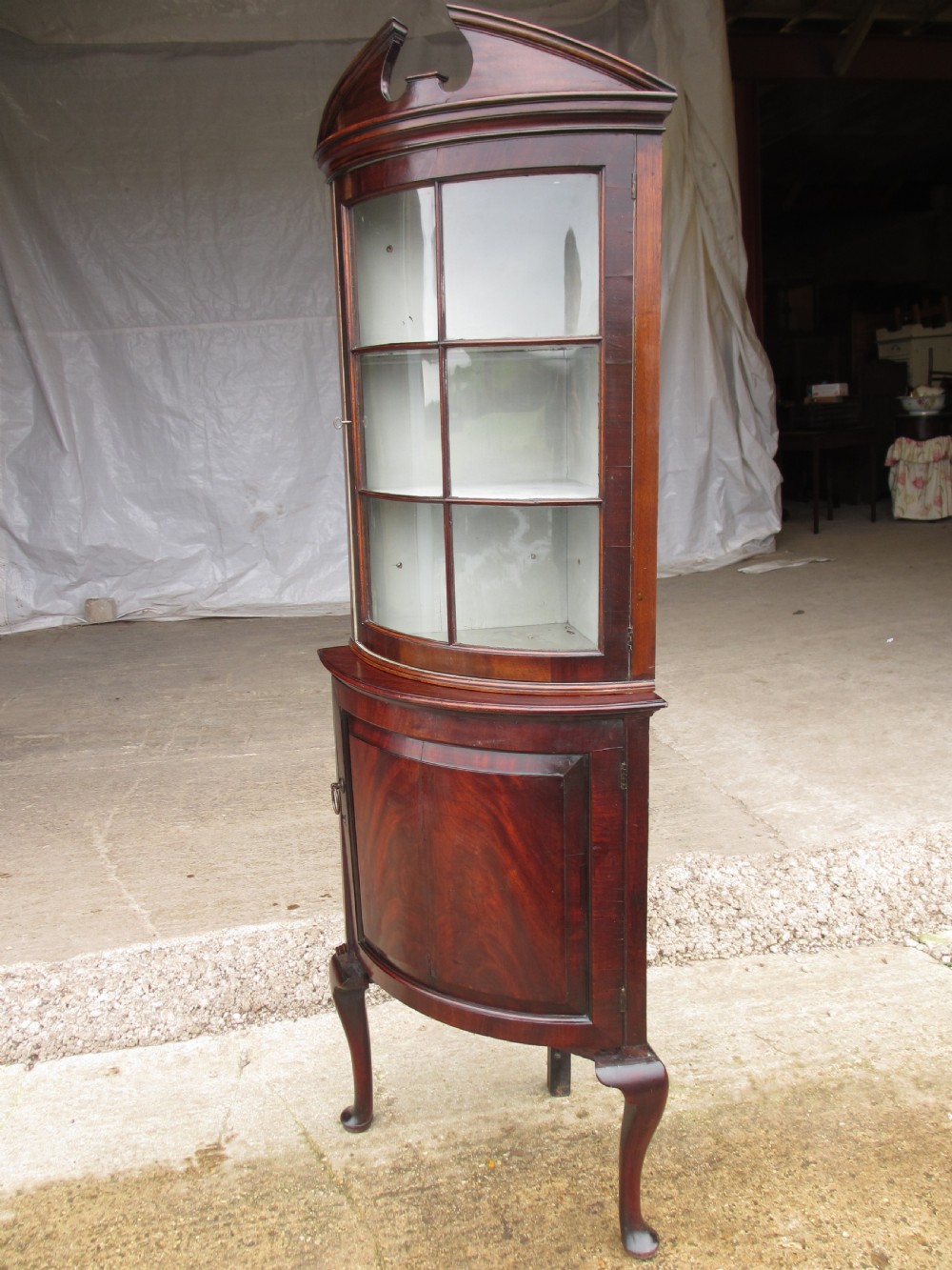 A two-piece flame mahogany corner cabinet featuring a broken pediment top, an upper glazed door, and a lower bow-front cupboard door supported by cabriole legs. View II