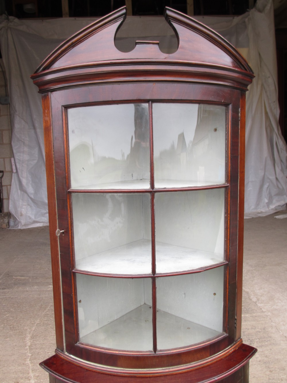 A two-piece flame mahogany corner cabinet featuring a broken pediment top, an upper glazed door, and a lower bow-front cupboard door supported by cabriole legs. View III