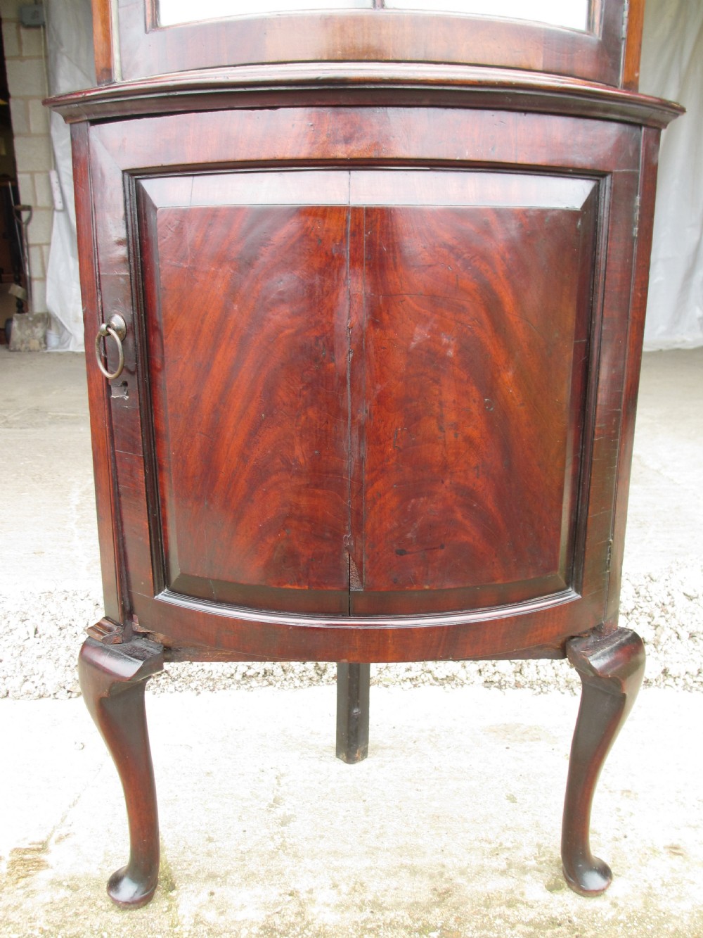 A two-piece flame mahogany corner cabinet featuring a broken pediment top, an upper glazed door, and a lower bow-front cupboard door supported by cabriole legs. View IV