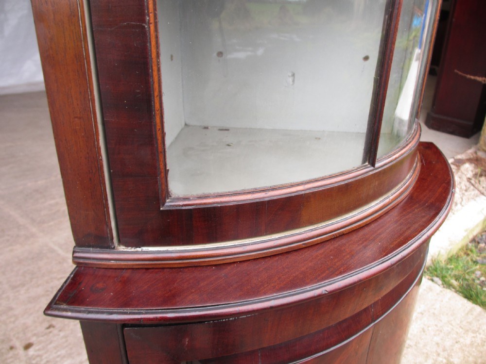 A two-piece flame mahogany corner cabinet featuring a broken pediment top, an upper glazed door, and a lower bow-front cupboard door supported by cabriole legs. View VII