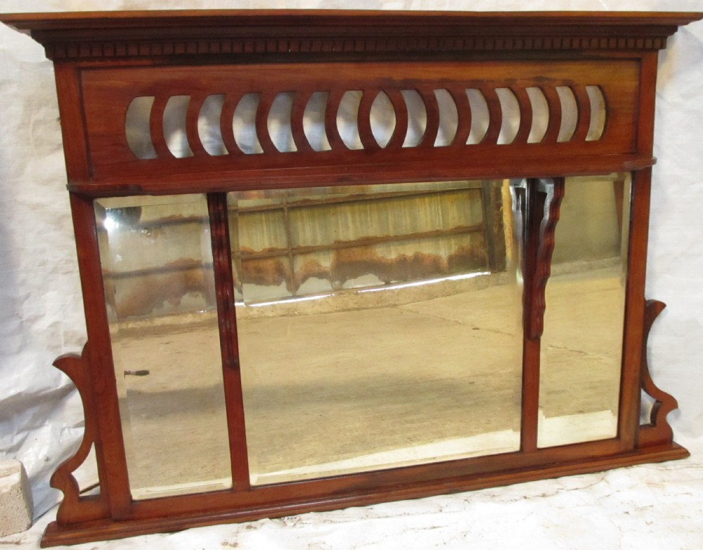 A Victorian mahogany triptych overmantel mirror featuring three glass panels, a fretted top frieze with crescent cut-outs, decorative side brackets, and a moulded cornice.
