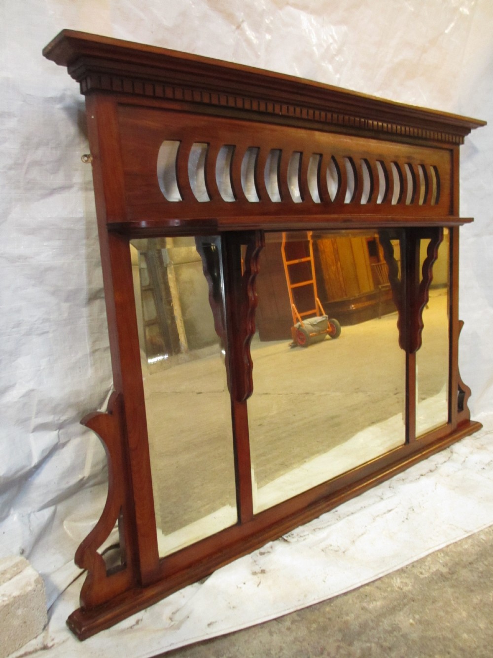A Victorian mahogany triptych overmantel mirror featuring three glass panels, a fretted top frieze with crescent cut-outs, decorative side brackets, and a moulded cornice. View II