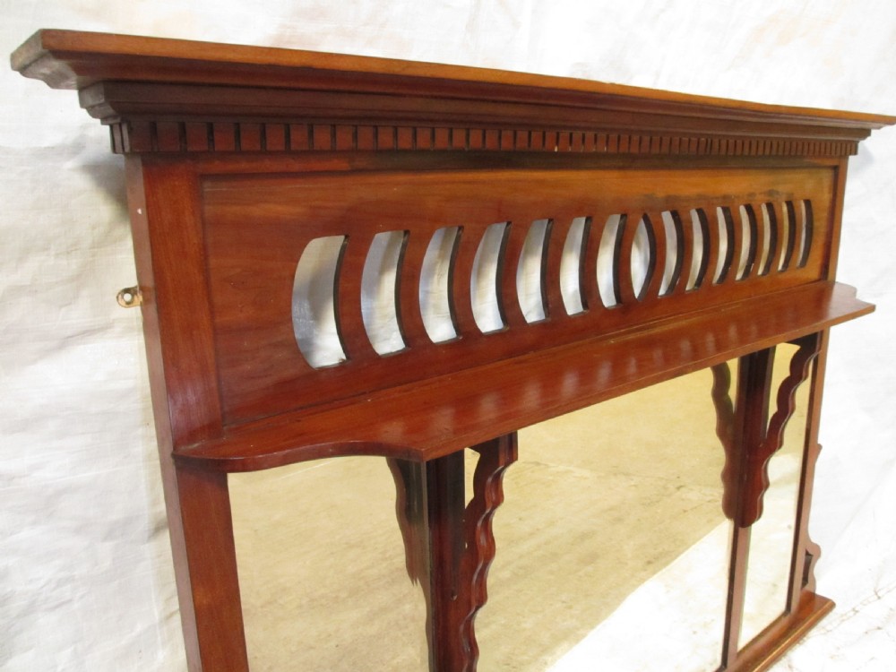 A Victorian mahogany triptych overmantel mirror featuring three glass panels, a fretted top frieze with crescent cut-outs, decorative side brackets, and a moulded cornice. View IV
