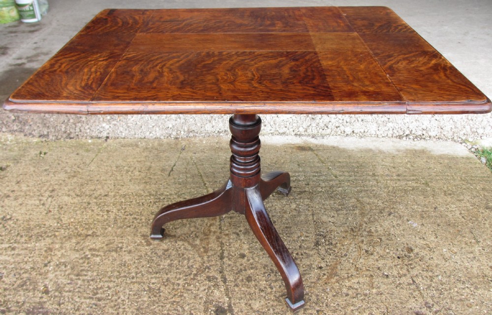A Victorian dark oak drop-leaf breakfast table featuring a rectangular surface with grain figure, a turned central pedestal stem, and splayed legs.