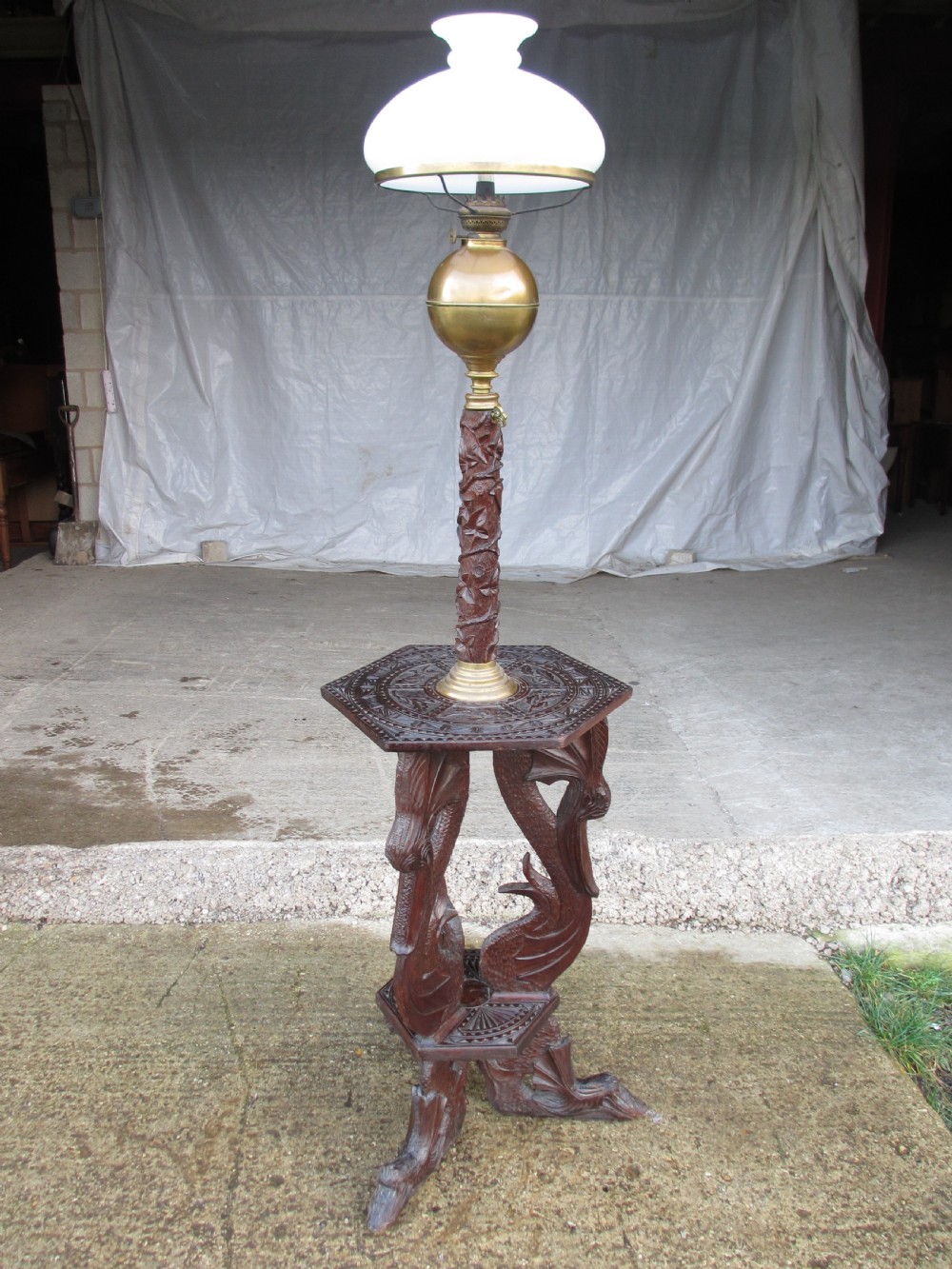 A Victorian Anglo-Burmese carved padouk wood and brass floor oil lamp with mythical dragon legs, a carved column, a brass reservoir, and a white glass shade. View II