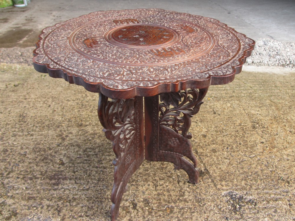 An Anglo-Indian carved teak occasional table with a scalloped circular top, floral inlay centre, and a folding fretted base.
