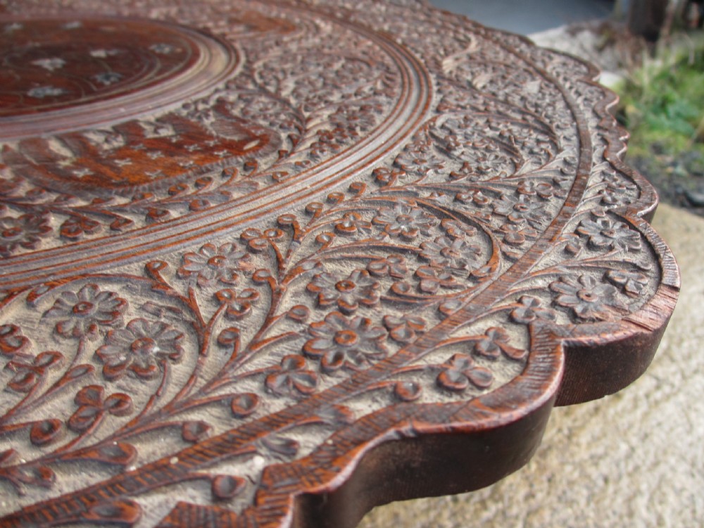 An Anglo-Indian carved teak occasional table with a scalloped circular top, floral inlay centre, and a folding fretted base. View IV