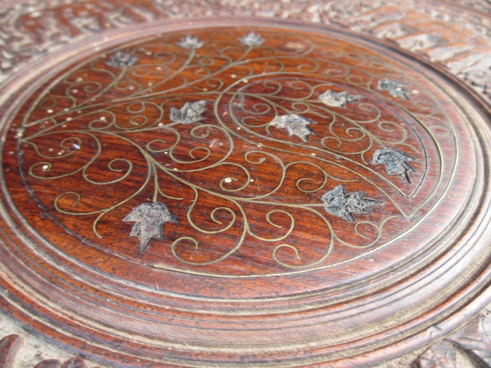 An Anglo-Indian carved teak occasional table with a scalloped circular top, floral inlay centre, and a folding fretted base. View VII