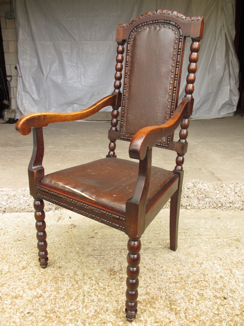 An Arts and Crafts mahogany carver armchair featuring bobbin-turned legs, curved armrests, a carved top crest, and brown studded leather upholstery. View III