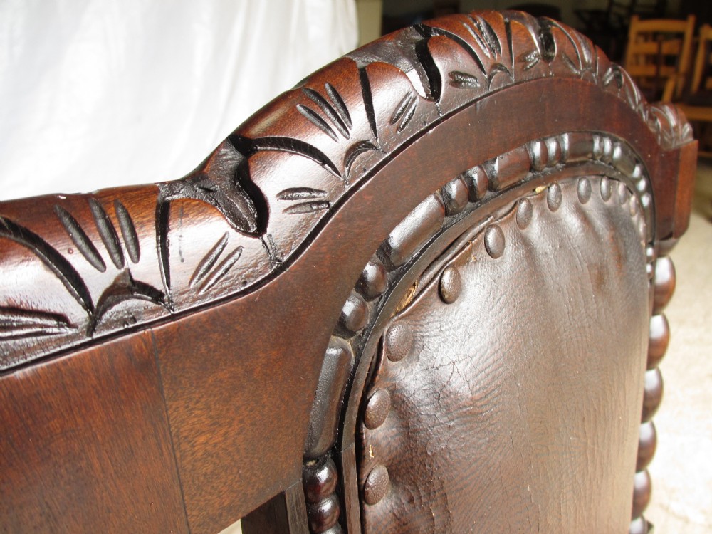 An Arts and Crafts mahogany carver armchair featuring bobbin-turned legs, curved armrests, a carved top crest, and brown studded leather upholstery. View V