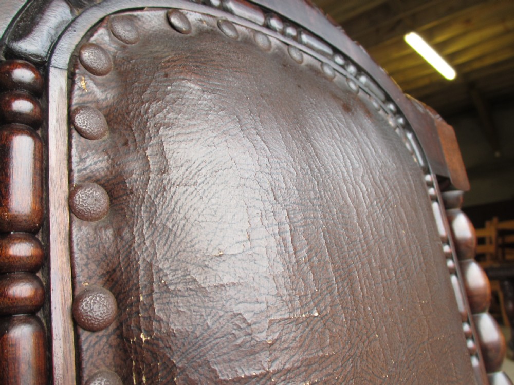 An Arts and Crafts mahogany carver armchair featuring bobbin-turned legs, curved armrests, a carved top crest, and brown studded leather upholstery. View VI