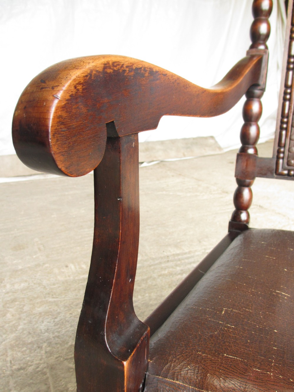 An Arts and Crafts mahogany carver armchair featuring bobbin-turned legs, curved armrests, a carved top crest, and brown studded leather upholstery. View VII
