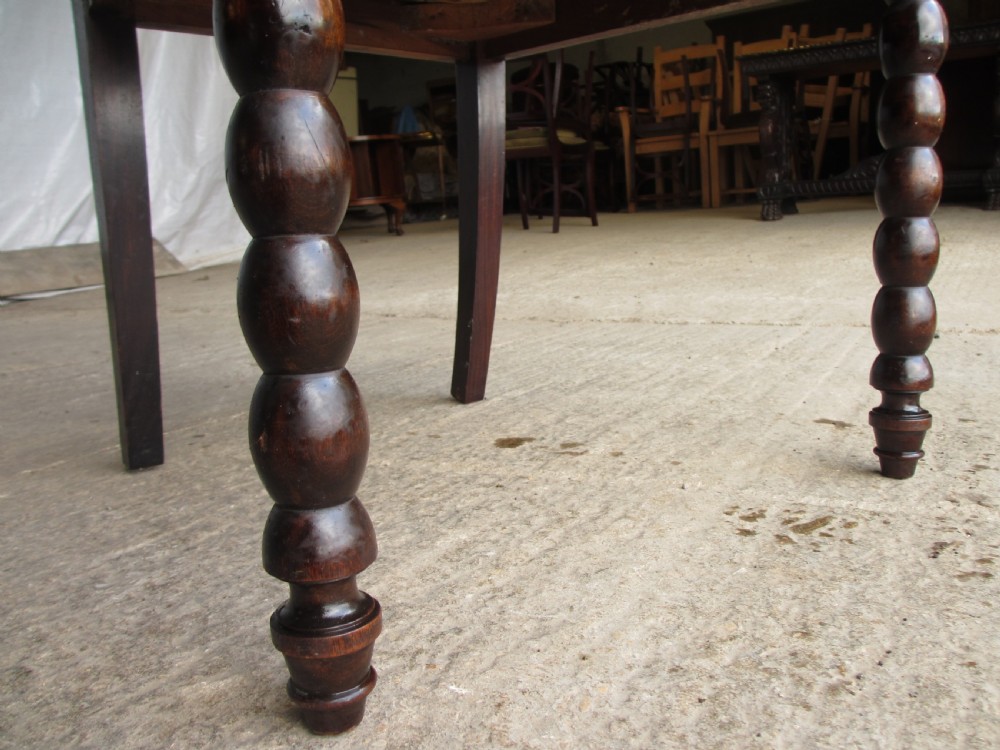 An Arts and Crafts mahogany carver armchair featuring bobbin-turned legs, curved armrests, a carved top crest, and brown studded leather upholstery. View IX