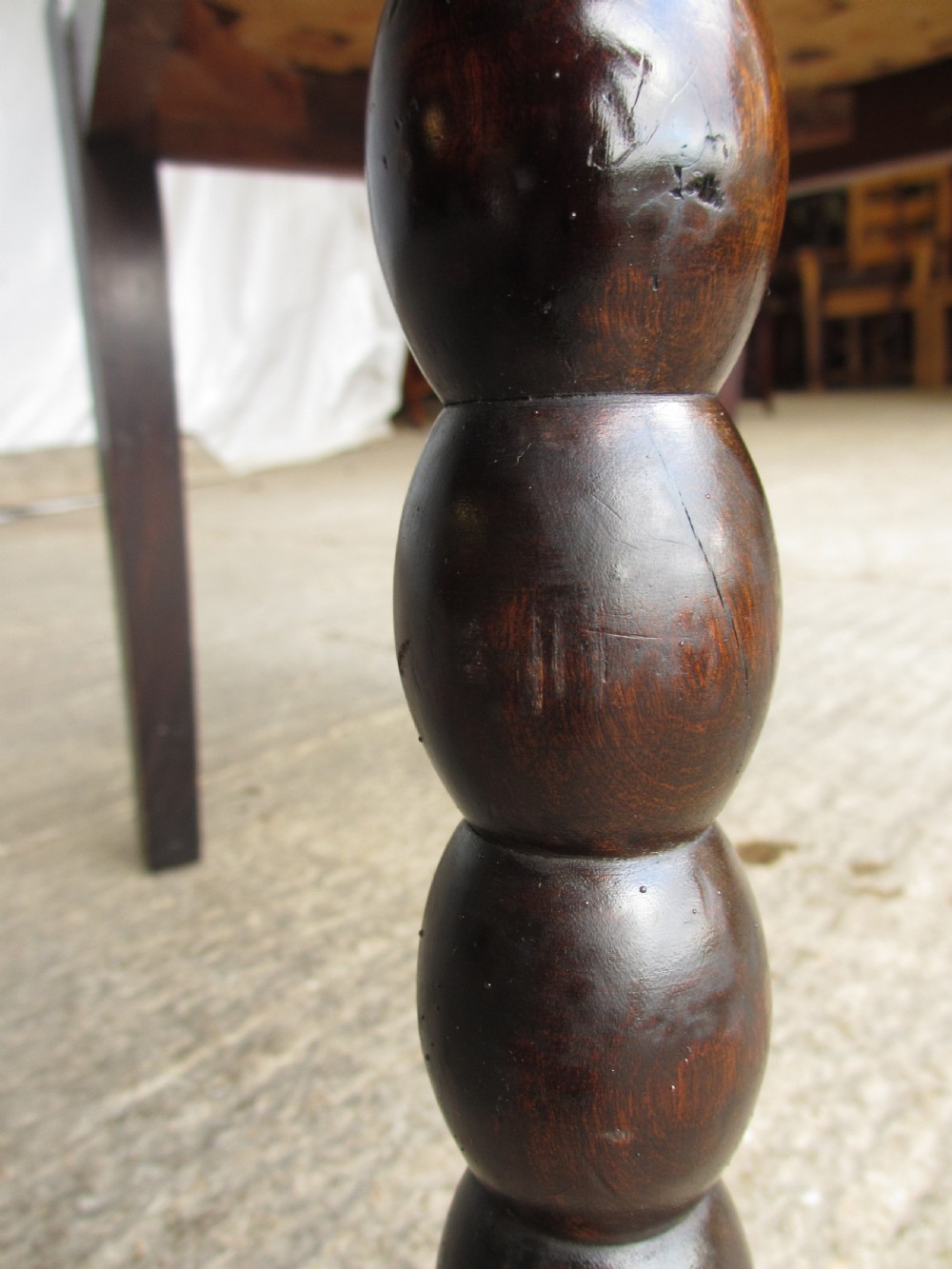 An Arts and Crafts mahogany carver armchair featuring bobbin-turned legs, curved armrests, a carved top crest, and brown studded leather upholstery. View X